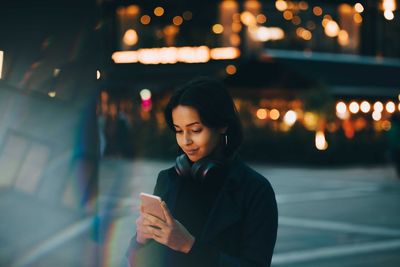 Young woman using mobile phone while standing in city at night