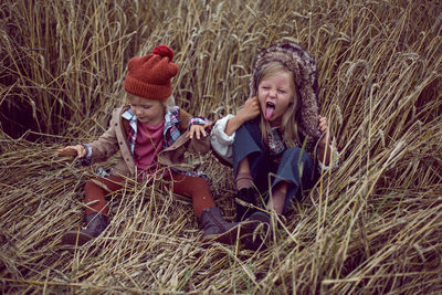 Two stylish sisters sitting in a field with wheat in the autumn