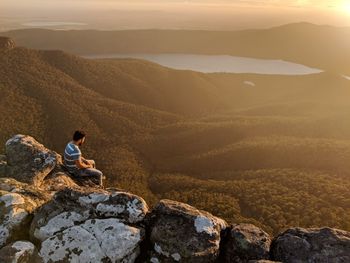 Rear view of man sitting on rock formation during sunset