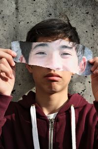 Close-up portrait of boy holding paper standing by wall