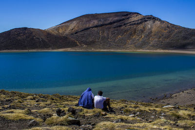 Rear view of people sitting by lake