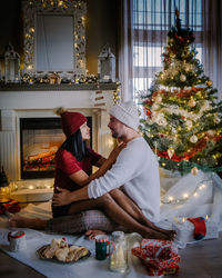 Couple sitting against christmas tree at home