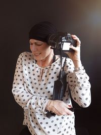 Young woman holding camera against black background