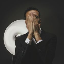 Tensed man covering of face against black background