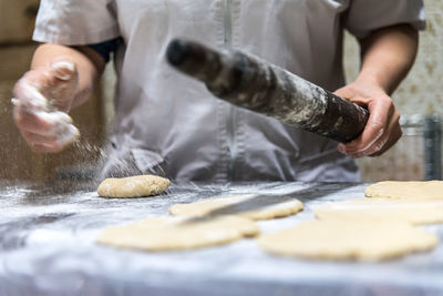 Unrecognizable baker with rolling pin spilling flour on table while preparing pastry in kitchen