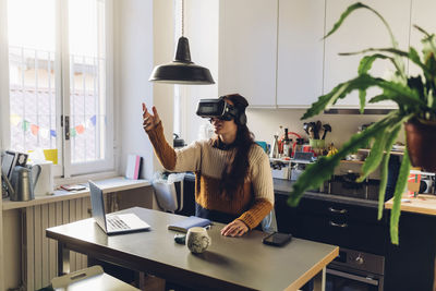 Woman gesturing wearing virtual reality headset at home