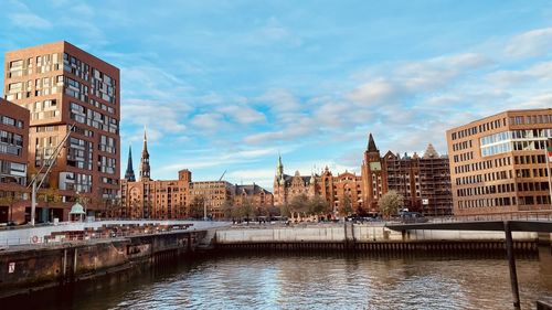 Buildings by river against sky