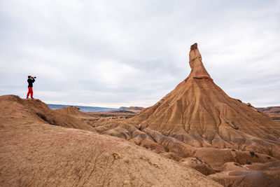 Side view of man photographing while standing on landscape against cloudy sky