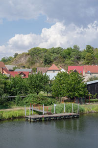 Trees and houses by river against sky