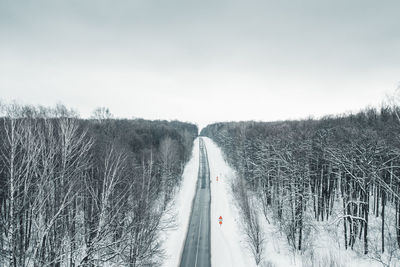 Road amidst trees on field against sky during winter