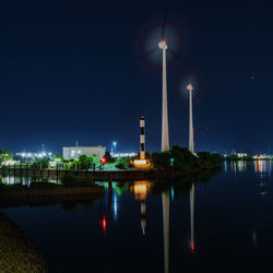 Illuminated building by river against sky at night