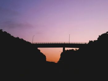 Silhouette bridge over river against sky during sunset