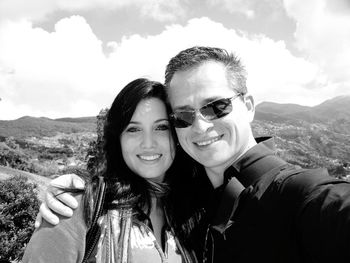 Portrait of happy couple standing on mountain against cloudy sky