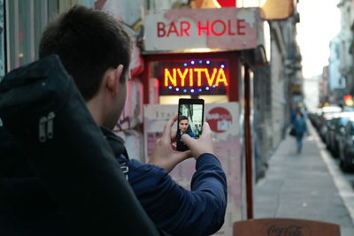 Close-up of young man taking selfie while standing on sidewalk in city