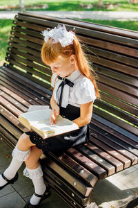 A child is sitting on a bench outside on a warm sunny day, and is returning to school. 