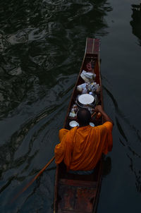 Rear view of monk sitting on boat in lake