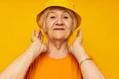 Portrait of senior woman wearing hat against yellow background