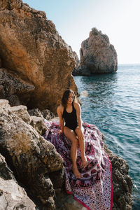 Woman sitting on rock by sea against clear sky