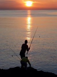 Silhouette man fishing in sea against sunset sky