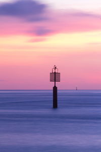 Lighthouse by sea against romantic sky at sunset