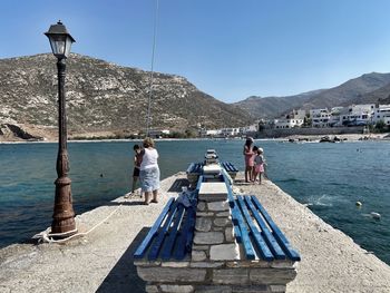 People on sea by mountains against clear sky