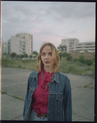 Portrait of beautiful young woman standing against sky in city