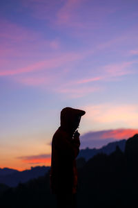 Silhouette man standing on mountain against orange sky