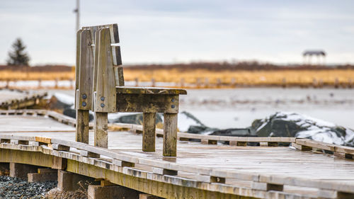 Wooden bench on boardwalk against sky