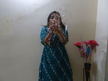 Woman holding umbrella standing against wall