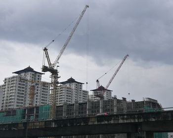 Low angle view of cranes against sky in city