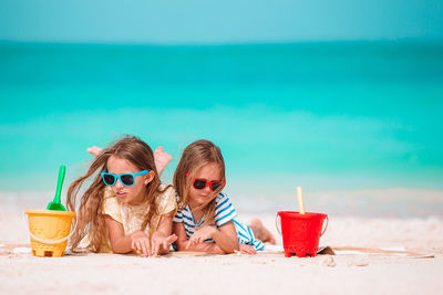 Cute girls lying down on beach against sky