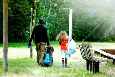 Rear view of father pulling bag while walking with daughter at park