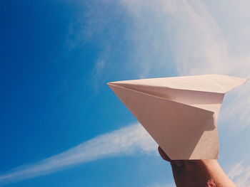 Low angle view of hand holding paper against blue sky