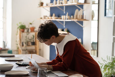 Focused artisan female pottery shop owner doing bookkeeping, measuring small business profitability