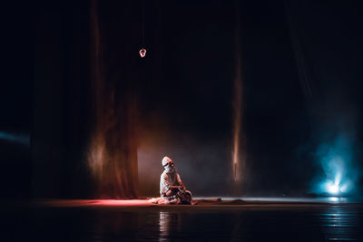 Blurred motion of man sitting on illuminated stage at night