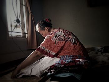 Side view of young woman sitting on bed at home