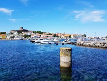 Sailboats in harbor by buildings against blue sky