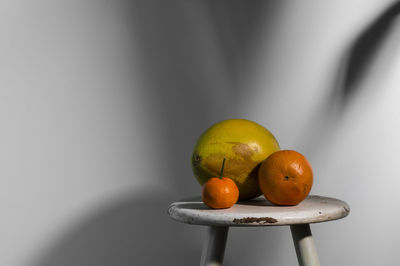 Still life of citrus fruits on white wooden stool against white wall with sunlight and shadow