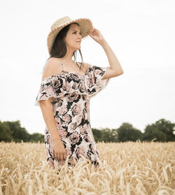 Beautiful woman wearing hat standing amidst crops on field