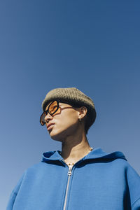 Low angle view of non-binary person looking away against clear blue sky