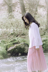 Side view of young woman standing by lake