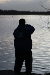 Rear view of man standing by lake against sky