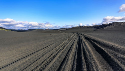 Tire tracks on desert against sky