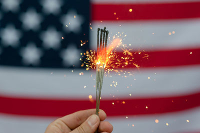 Cropped hand of person holding illuminated sparklers against american flag