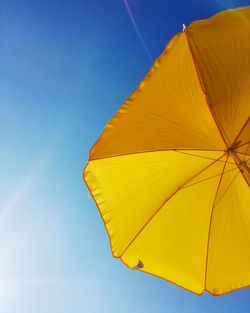 Low angle view of yellow umbrella against blue sky