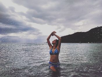 Full length of shirtless young woman standing in sea against sky