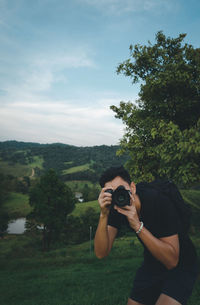 Man photographing through camera while standing on field against sky