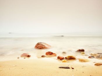 Romantic sunset at horizon, reflecting on smooth stony shore with big boulders, wavy baltic sea