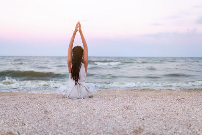 Woman doing yoga at beach against sky during sunset