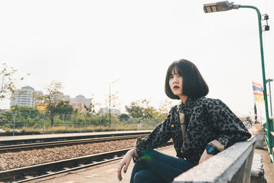 Full length of woman sitting on bench at railroad station platform
